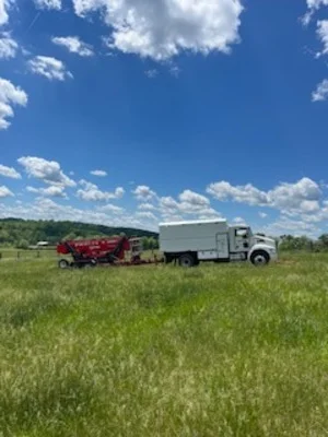 Red wood chipper and white dump truck processing tree debris in field